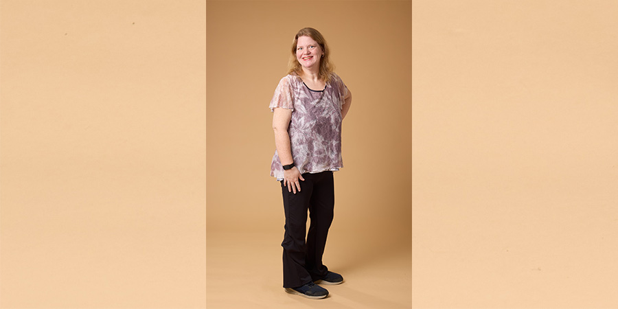 Jennifer posing for COMP photo shoot. She is a white woman wearing black pants and a purple, flowy top.