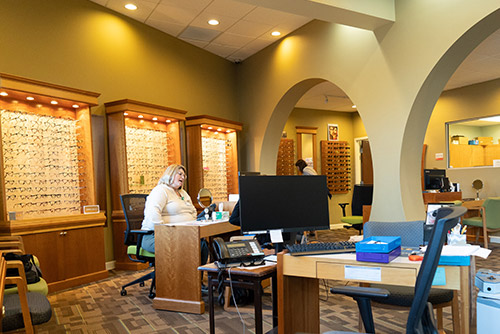 Eye care clinic with glasses displays and a staff member at a desk.